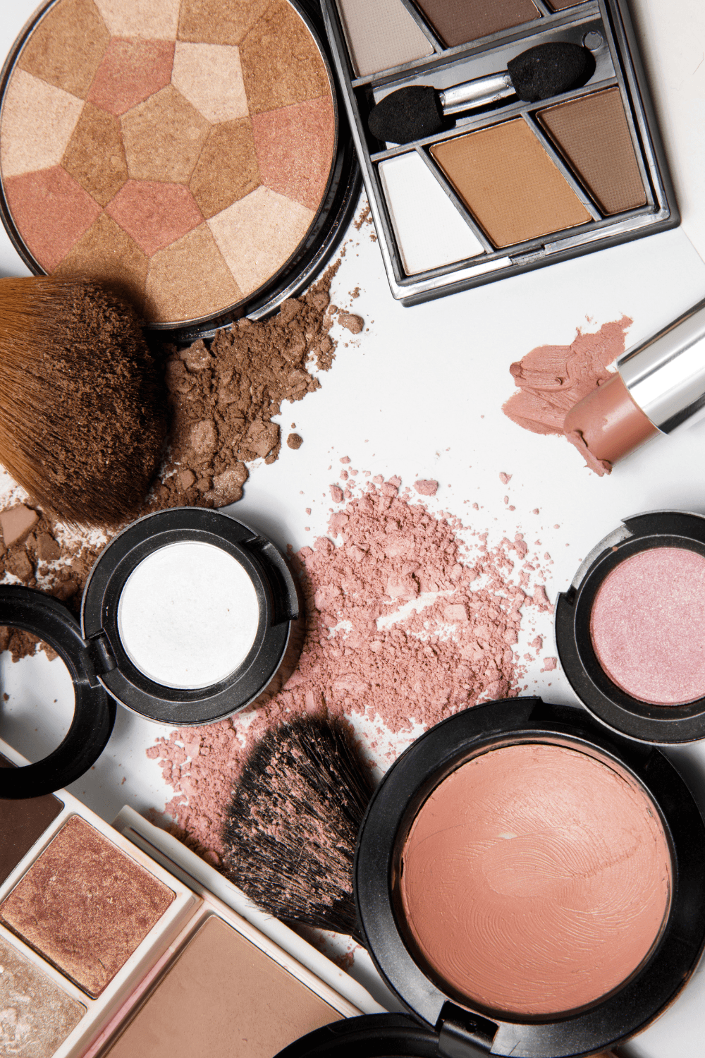 Surtido de productos de maquillaje que incluye colorete, sombra de ojos, polvos compactos, pintalabios y brochas dispuestos sobre una superficie blanca, perfectos para ideas de maquillaje o para crear tu look de maquillaje para Acción de Gracias