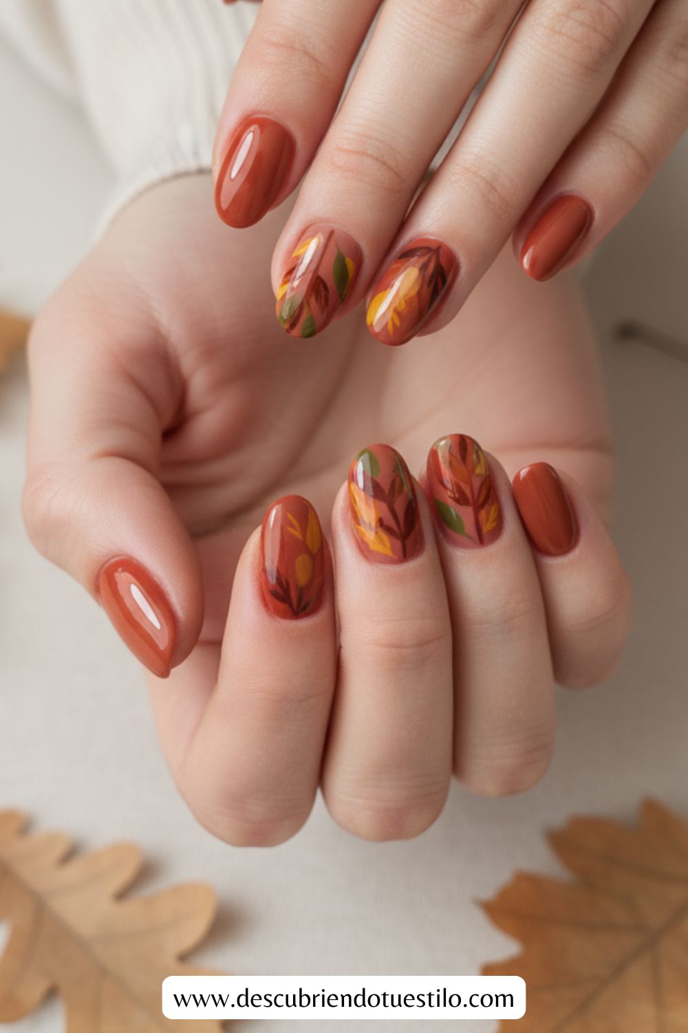 Manos con uñas elegantes en tonos otoñales de marrón, naranja y amarillo, con diseños de hojas